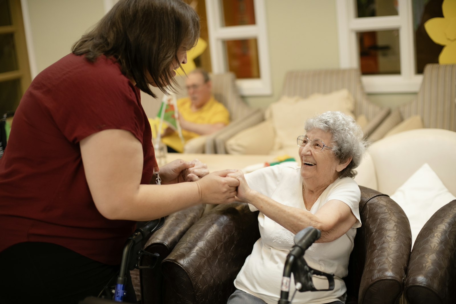 Caregiver holding hands with a smiling senior woman in a care home lounge